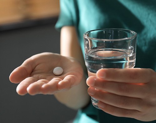Person with a glass of water and pill in their hand