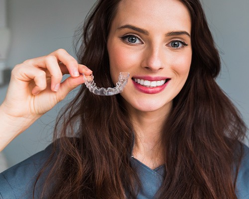 A young woman holding up a nearly invisible Invisalign tray