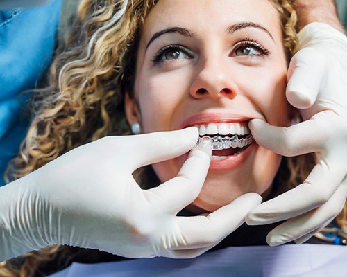 A dentist placing a woman’s new Invisalign trays