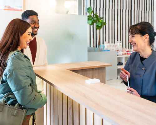 Dental receptionist smiling at couple in lobby