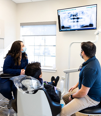 Dentist with a patient and team member looking at dental x rays