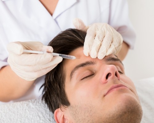 Man relaxing with eyes closed while a person wearing gloves injects Botox into his forehead