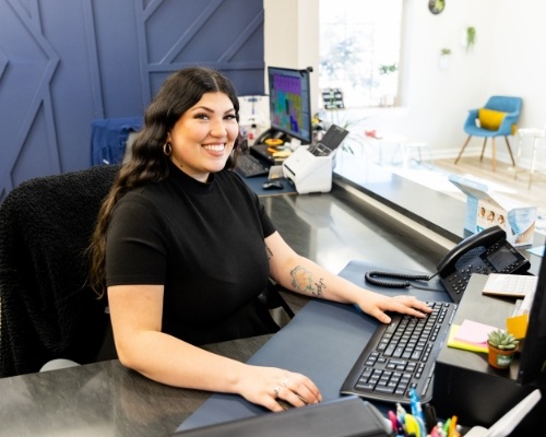 Smiling dental team member sitting in front of computer at front desk