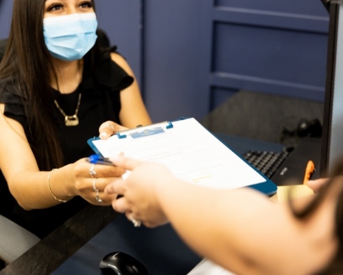 Dental team member handing a clipboard with forms to a patient