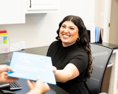 Smiling dental team member taking a clipboard from a patient