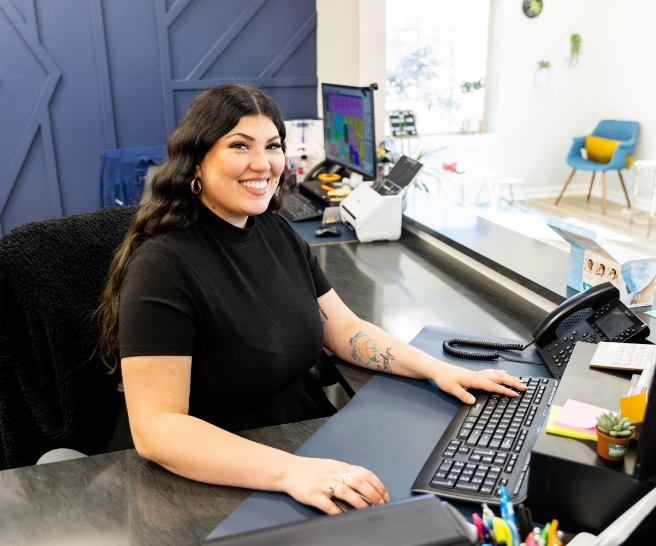 Smiling Jenks dental team member sitting in front of computer at front desk