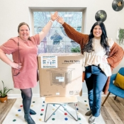 Two Jenks dental team members gesturing to a cardboard box containing a fire pit table