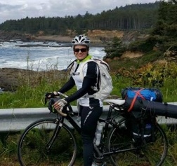 Doctor Schuyler standing with her bike by a highway rail with trees and pond in background