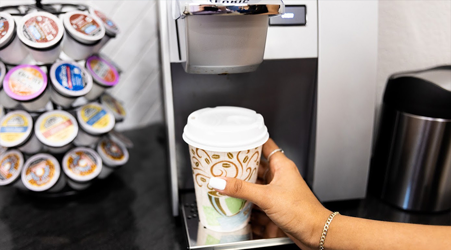 Person filling up a plastic cup at coffee machine in Jenks dental office