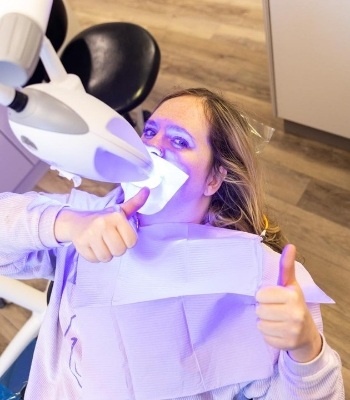 Woman giving thumbs up while getting teeth whitening from cosmetic dentist