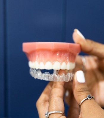 Person placing an Invisalign clear aligner over a model of a row of teeth
