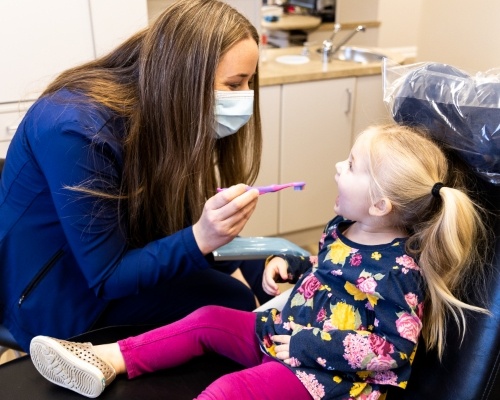 Dental team member about to brush the teeth of a young girl in the dental chair