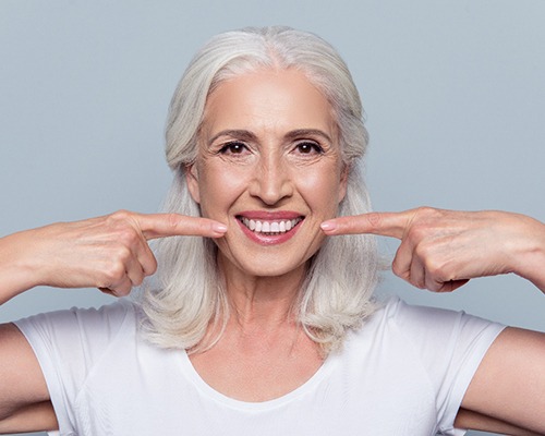 Woman with white hair pointing to her smile with both hands