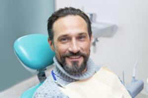 Older man in gray sweater in dentist's chair smiling